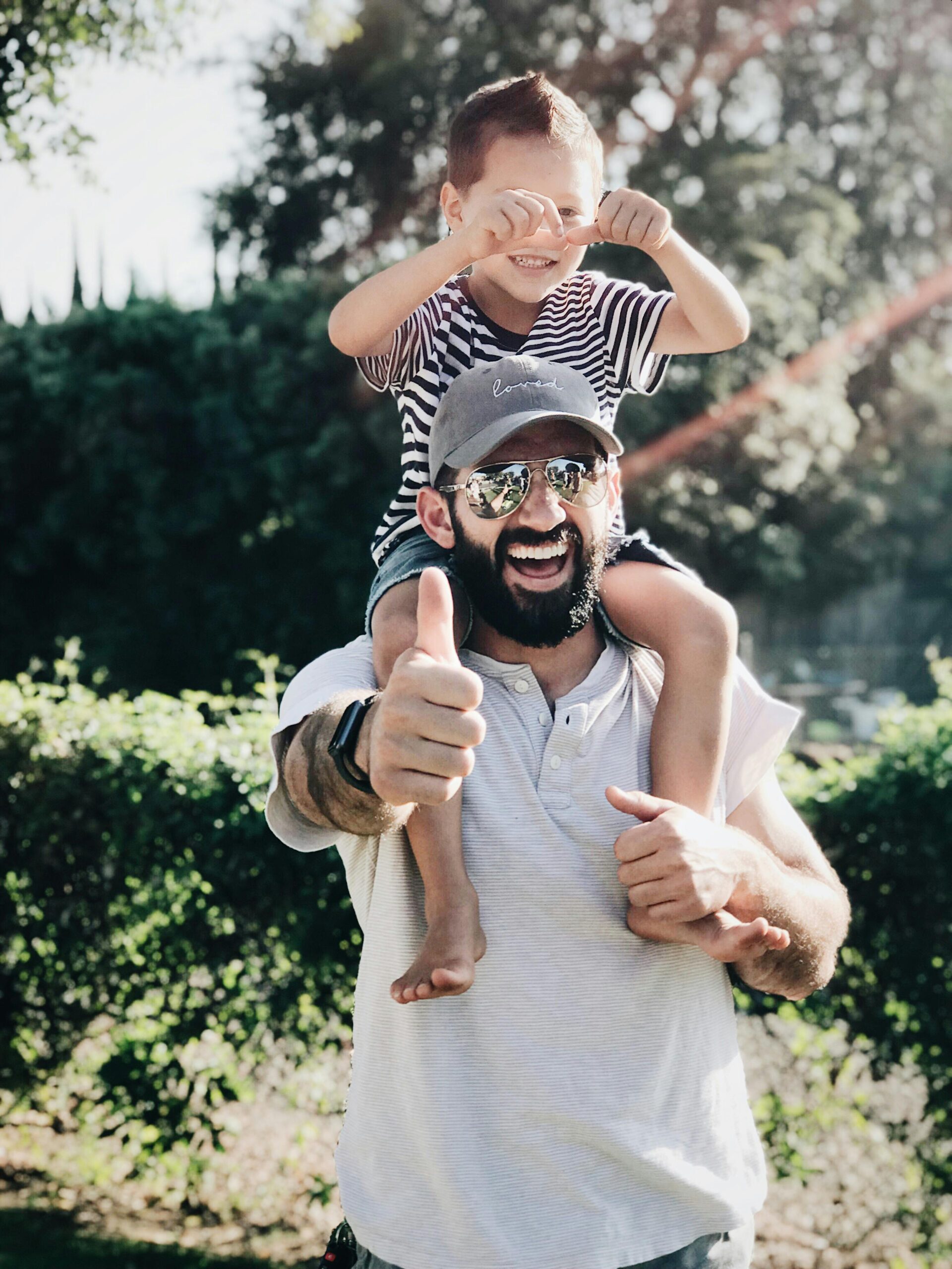 Home Father giving son a ride on shoulders, both laughing and smiling in a park setting.
