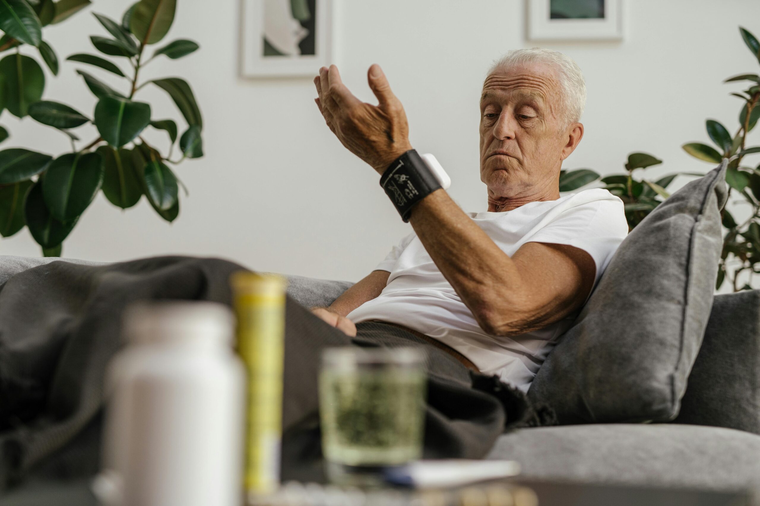 Home Elderly man checks his blood pressure using a wrist monitor in a comfortable living room setting.